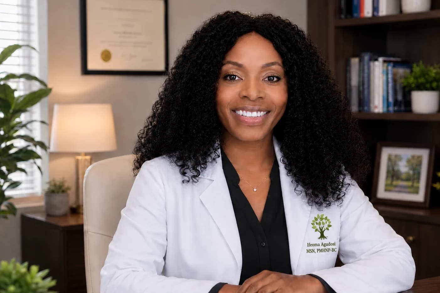 Ify Agudosi, MSN, PMHNP-BC, seated at her desk in a white coat, smiling, bookshelves and a lamp behind her.